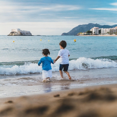 fotografía de lejos de niños y niñas jugando en el agua, de espaldas a la cámara, en la playa
